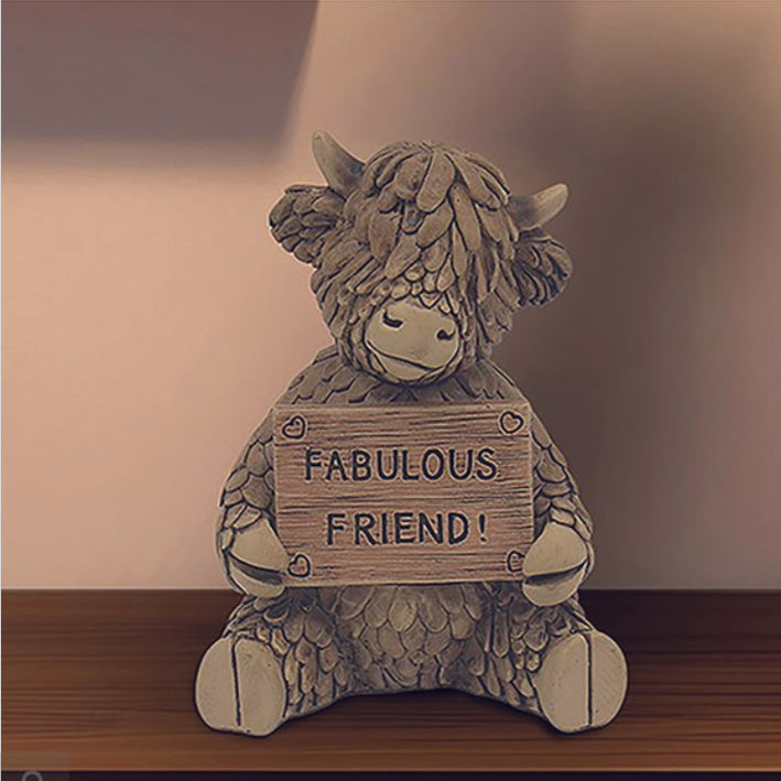 Hughie the Highland Cow, sitting holding Fabulous Friend sign ornament